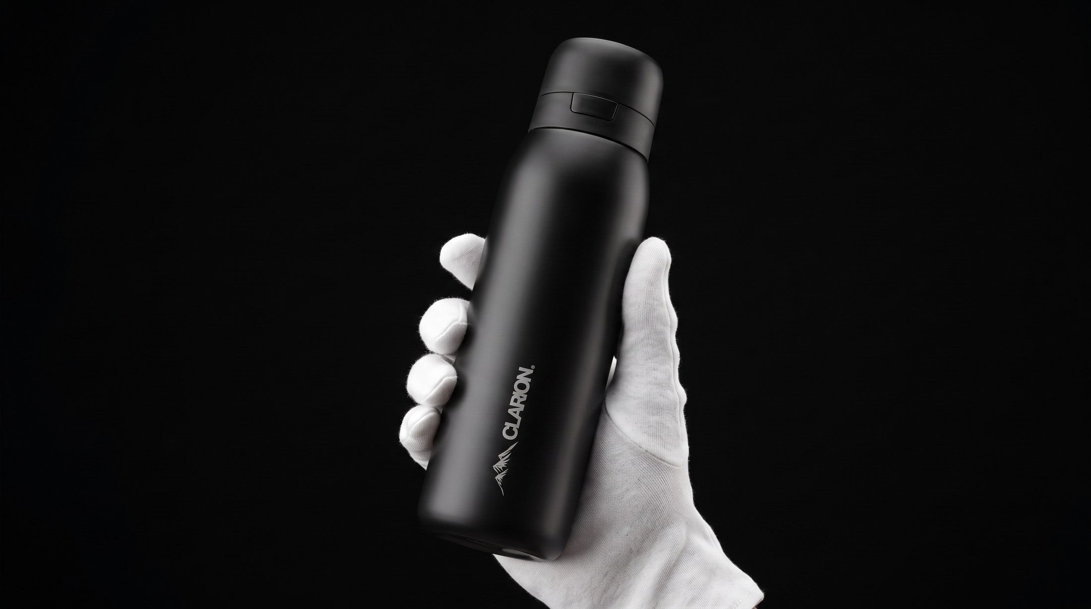 Clarion Bottle in matte black, held in a white-gloved hand against a black backdrop
